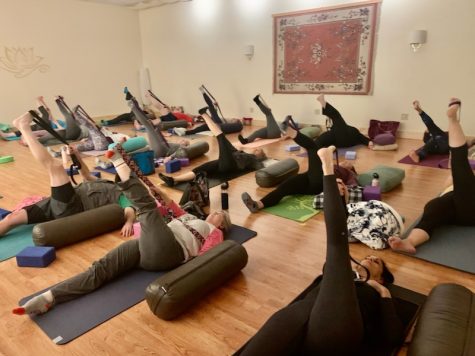 Yogis do a supported pose that helps with opening up the hips, glutes, and hamstrings during a class at Stoughton Yoga.